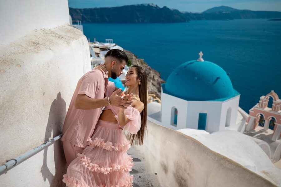A couple in a long dress on a terrace above the blue domes of Oia, Santorini